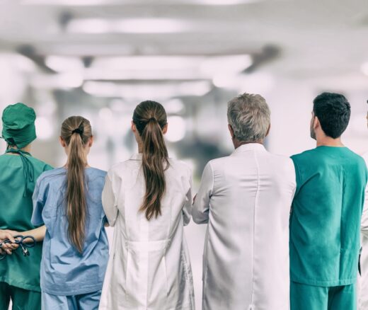 A team of clinicians in the ER standing shoulder-to-shoulder with their backs facing the camera.
