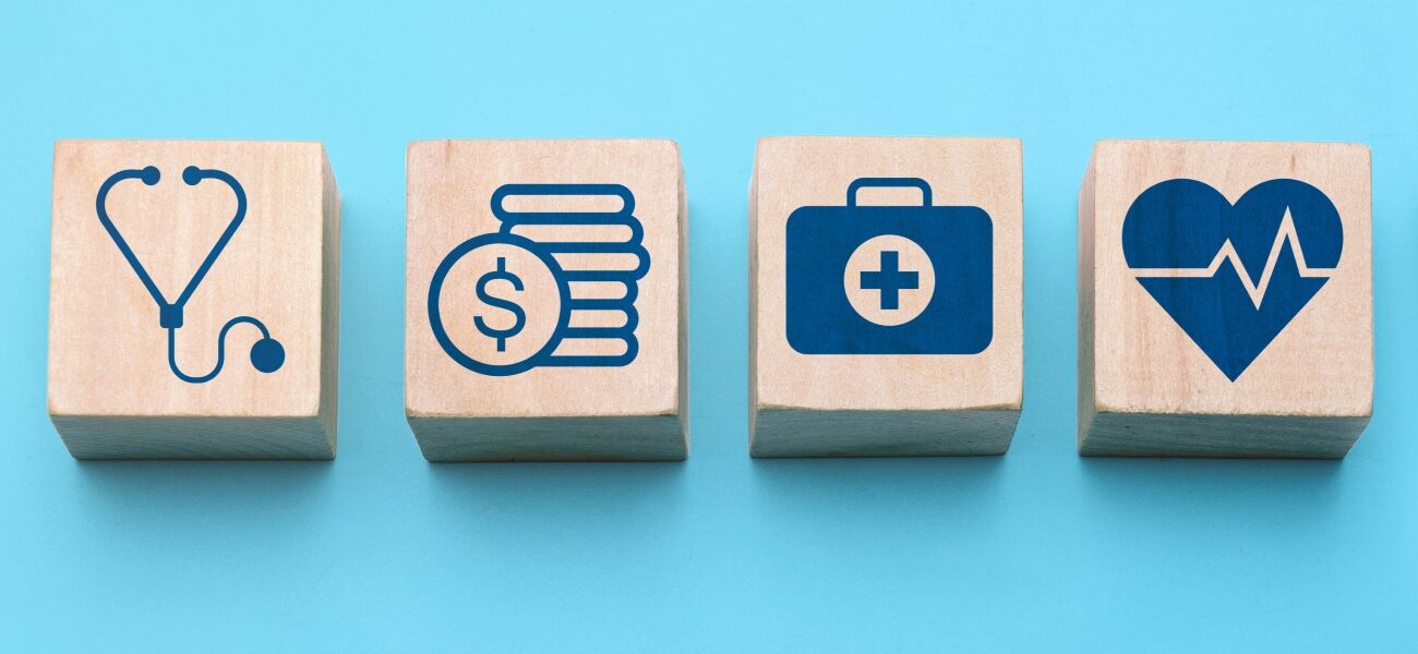 Healthcare planning and medical insurance concept with hand arranging wooden blocks showing icons of stethoscope, finance, first aid, heart health, and cross symbol on blue background