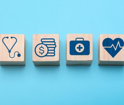 Healthcare planning and medical insurance concept with hand arranging wooden blocks showing icons of stethoscope, finance, first aid, heart health, and cross symbol on blue background