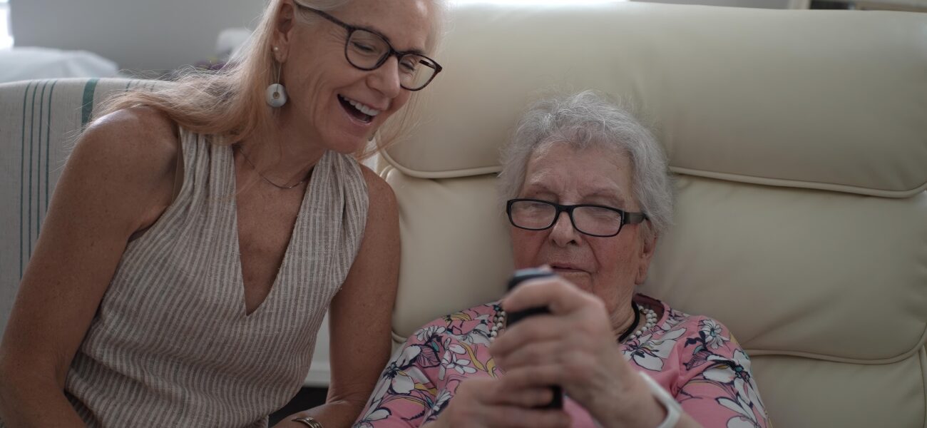 Smiling daughter helps elderly mother with phone