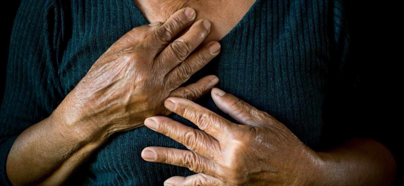Older Black woman with hands on chest on black background