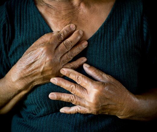 Older Black woman with hands on chest on black background