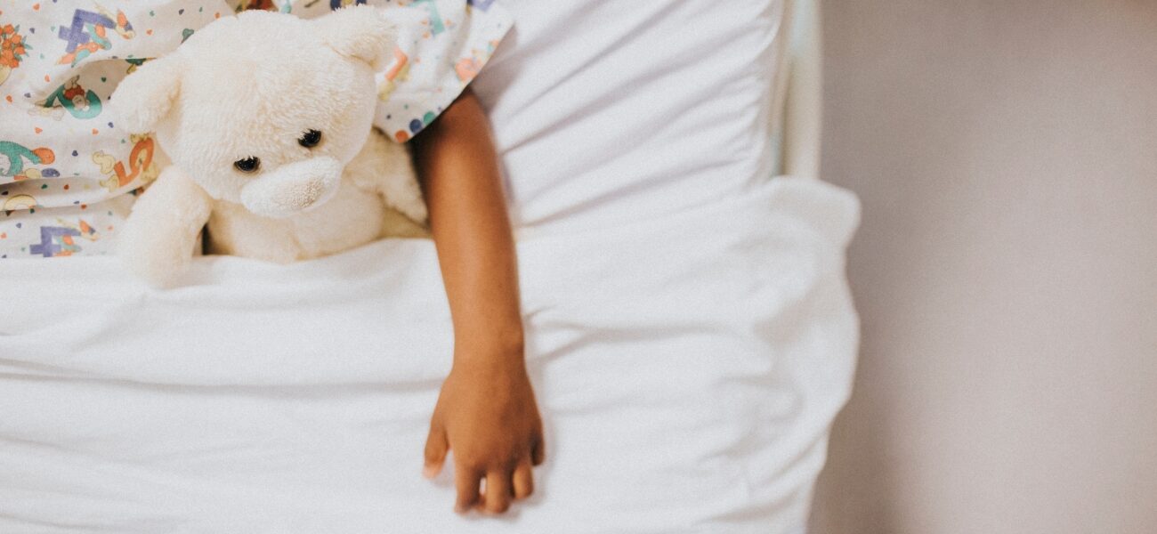 A Black child in a hospital bed with a stuffed animal.