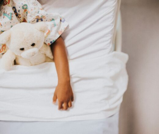 A Black child in a hospital bed with a stuffed animal.