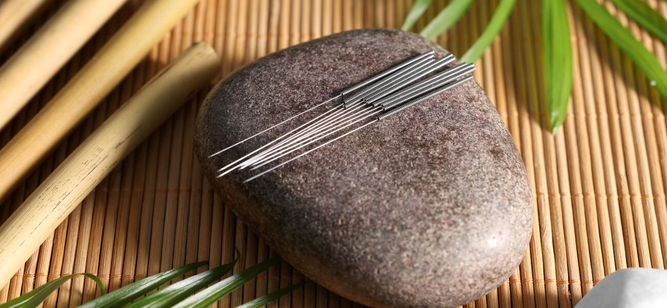 Stone with acupuncture needles on bamboo mat, above view