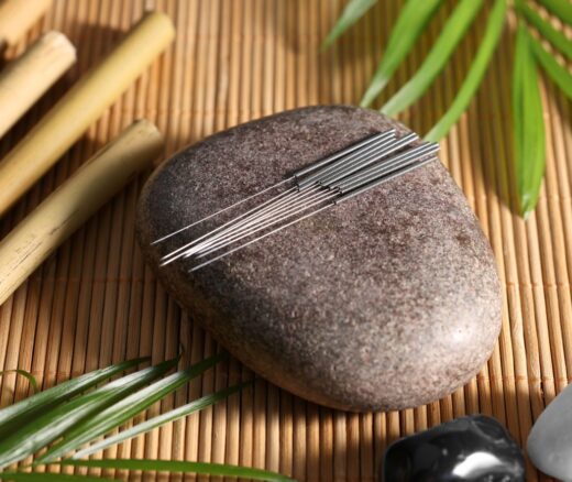 Stone with acupuncture needles on bamboo mat, above view
