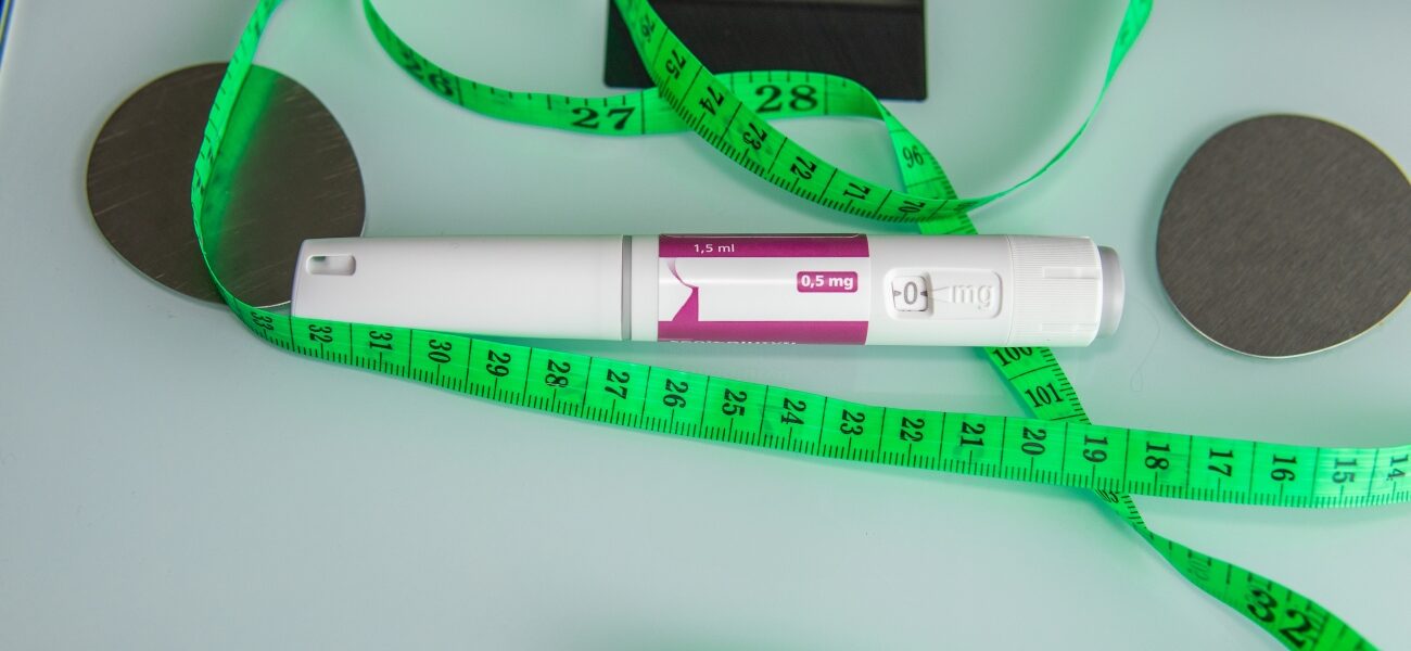 A GLP-1 injection laying atop of a scale and a green measuring tape.