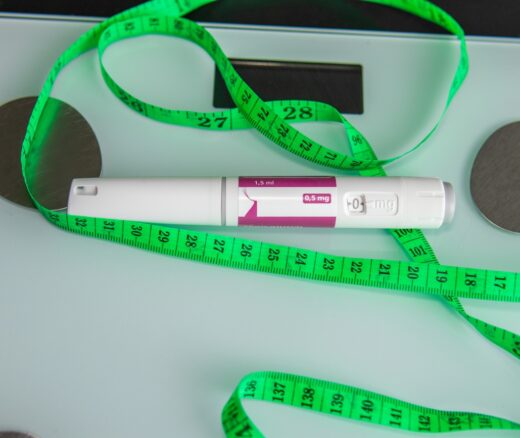 A GLP-1 injection laying atop of a scale and a green measuring tape.