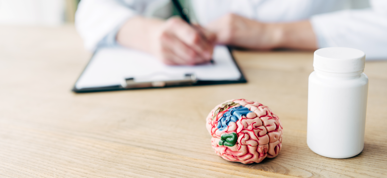 Model of a brain next to a blank pill bottle with a doctor in the background.