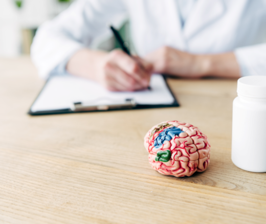 Model of a brain next to a blank pill bottle with a doctor in the background.