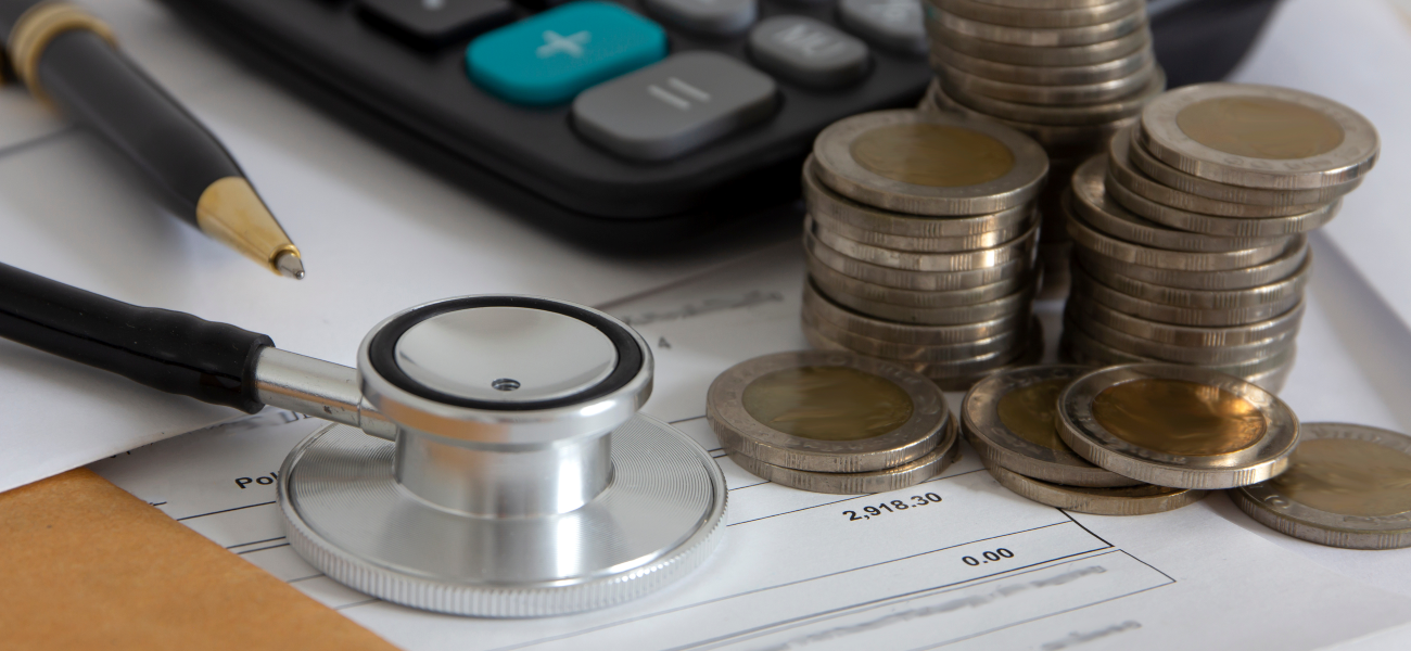 A stethoscope, pen, and calculator laying on a bill with coins.