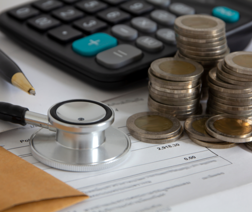 A stethoscope, pen, and calculator laying on a bill with coins.