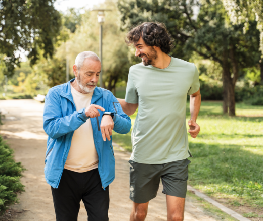 An older adult walking with a younger adult looking at his smart watch.