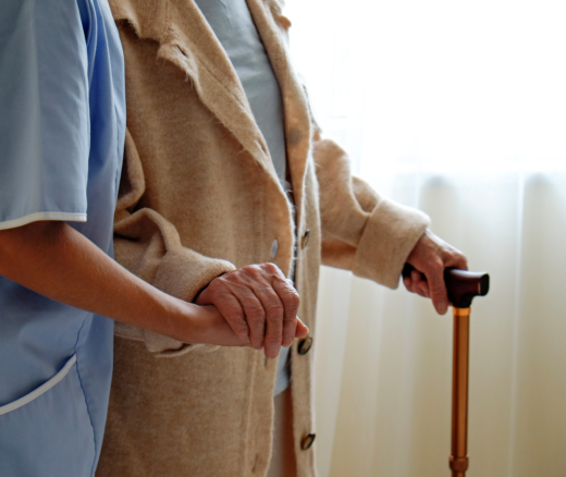 Nursing home staff member holds hand of resident with a cane.