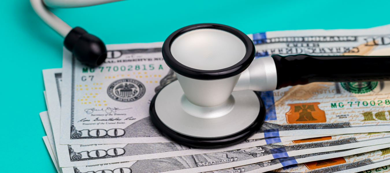Six $100 bills on a teal background with a stethoscope resting on top.