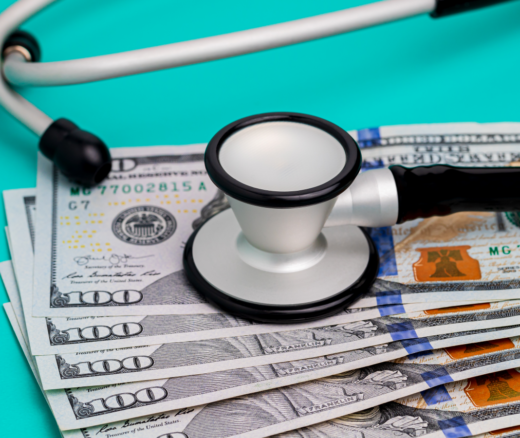 Six $100 bills on a teal background with a stethoscope resting on top.