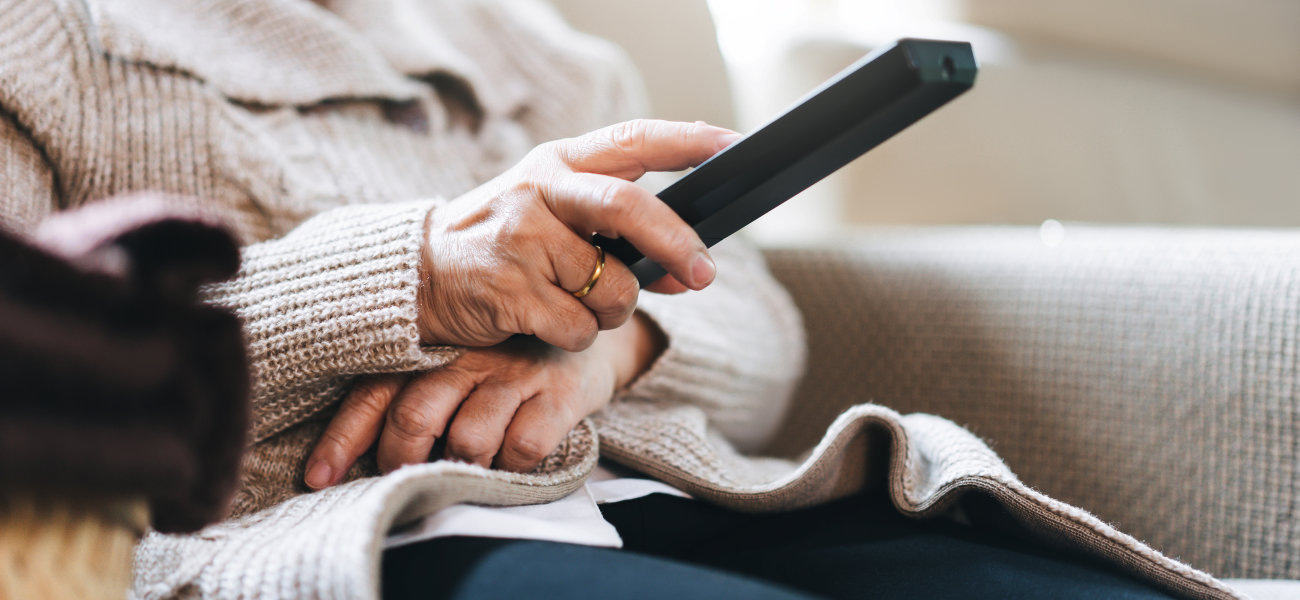 An elderly person sitting on the cough holding a TV remote.