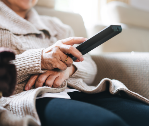 An elderly person sitting on the cough holding a TV remote.