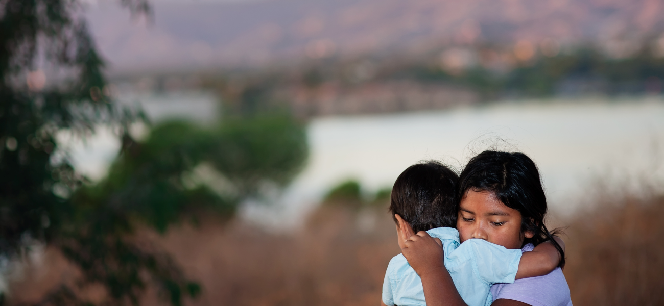 Brother and sister separated from parents are hugging each other near a river.