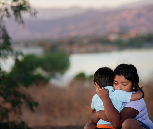 Brother and sister separated from parents are hugging each other near a river.