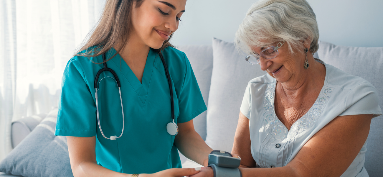 A nurse measuring an elderly woman's blood pressure sitting on a couch.