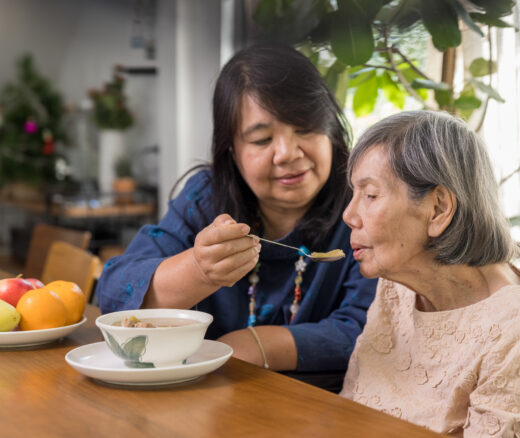 Daughter feeding elderly mother with soup.