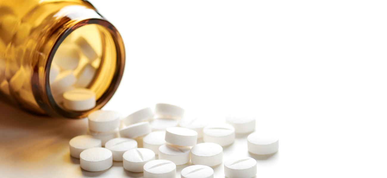 An image of white pills spilling out of a bottle onto a white surface