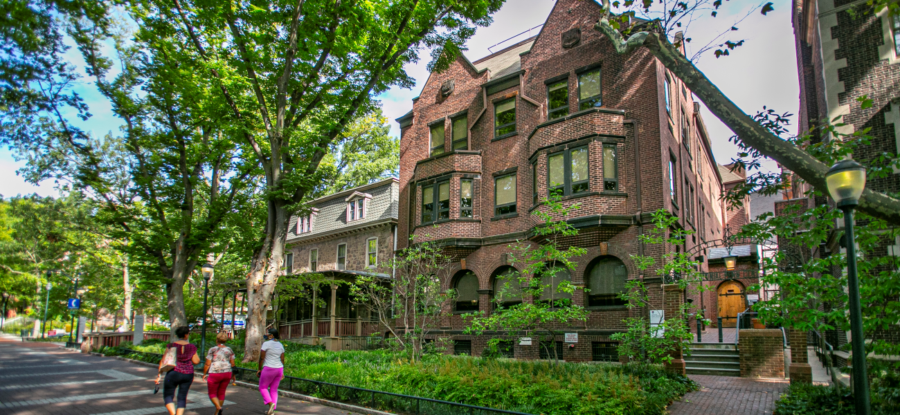 The exterior of Colonial Penn Center on Locust Walk. Building is surrounded by green trees and a lawn.