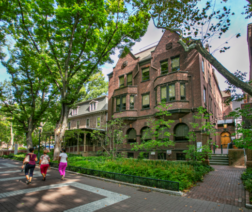 The exterior of Colonial Penn Center on Locust Walk. Building is surrounded by green trees and a lawn.