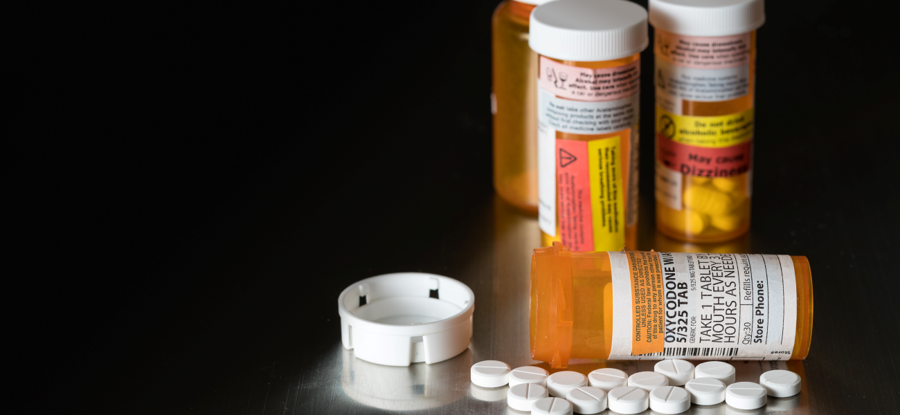 Three bottles of opioid prescriptions, and one bottle on its side laying next to white pills.