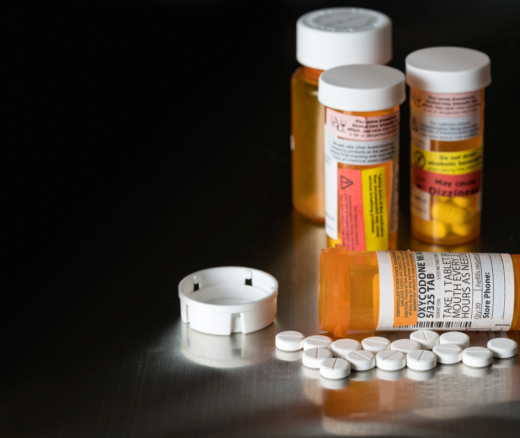 Three bottles of opioid prescriptions, and one bottle on its side laying next to white pills.
