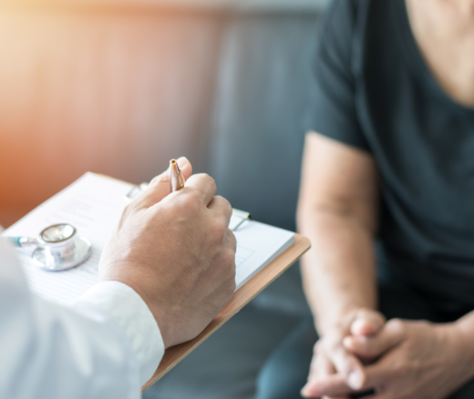 A doctor with a clipboard and stethoscope facing a patient wearing a plain T-shirt.