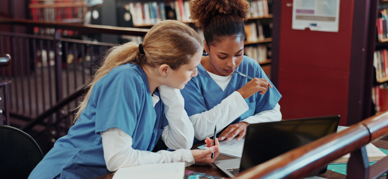 Two women in medical scrubs studying in a university library.