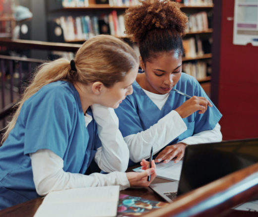 Two women in medical scrubs studying in a university library.