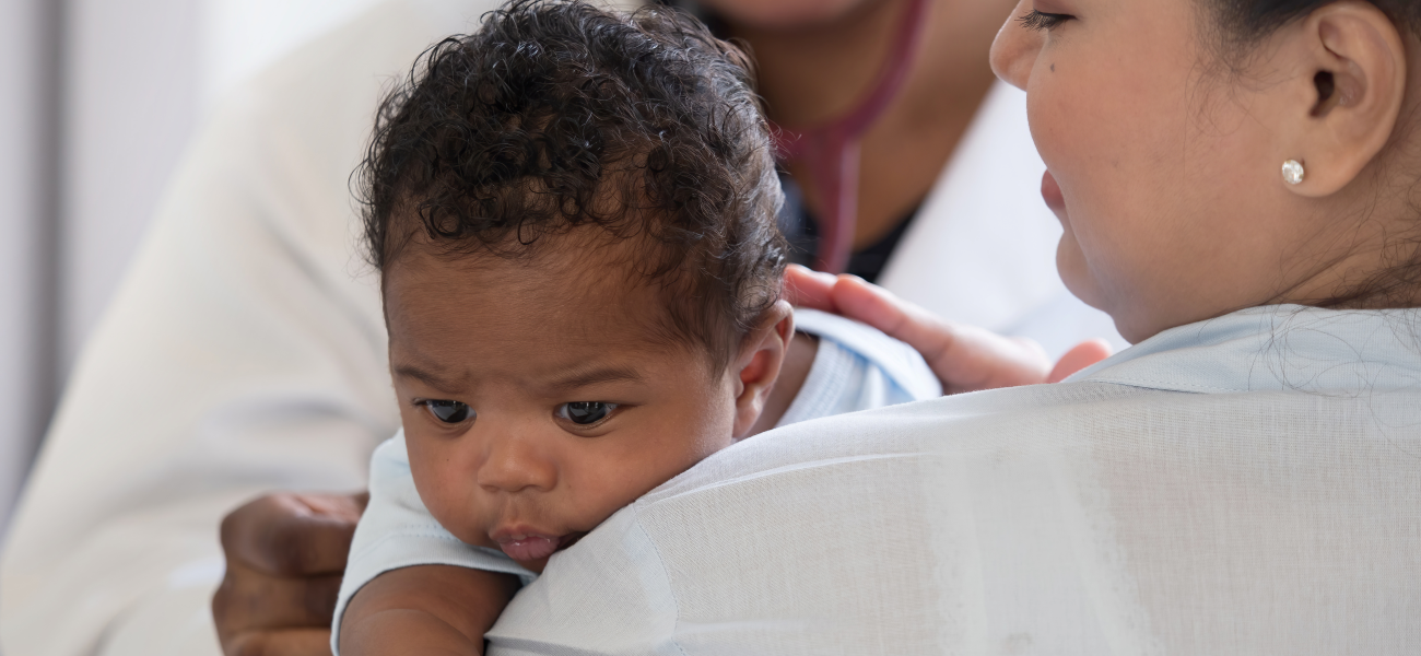 An infant held by their mother getting a check up by a doctor.