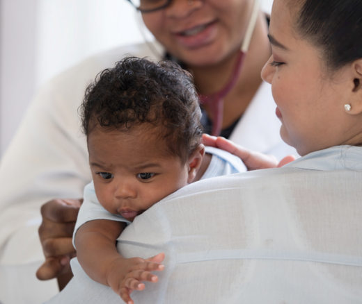 An infant held by their mother getting a check up by a doctor.