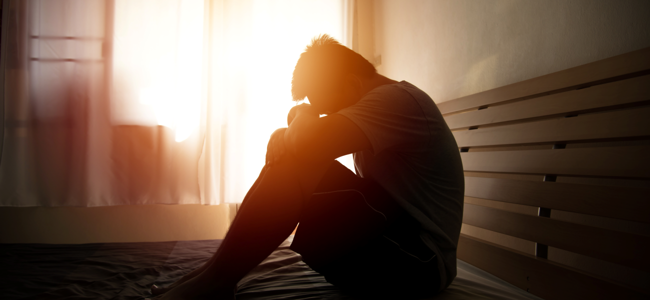 A person in anguish sitting on a bed as the sun rises.