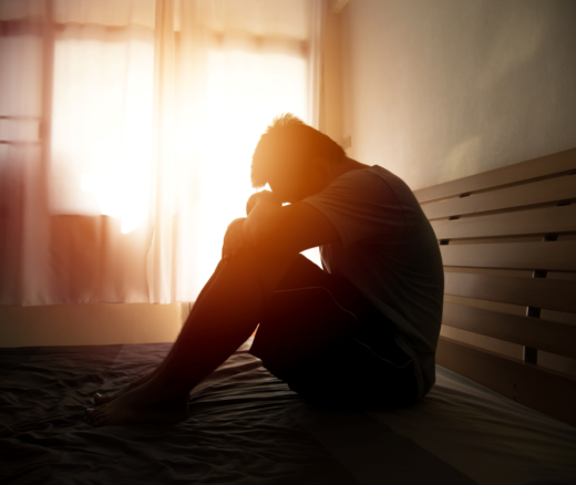 A person in anguish sitting on a bed as the sun rises.