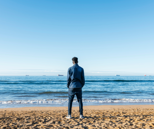 An African man on the beach looking at the ocean from behind.