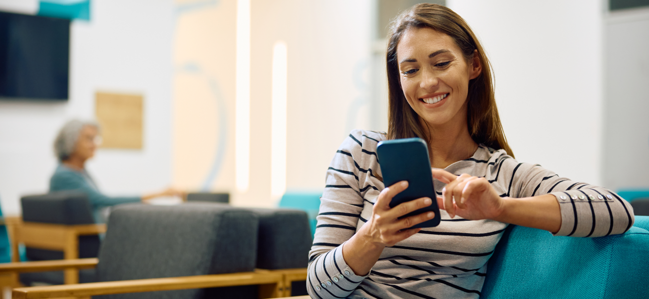 Smiling woman texting on mobile phone while waiting for medical appointment at clinic.