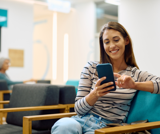 Smiling woman texting on mobile phone while waiting for medical appointment at clinic.